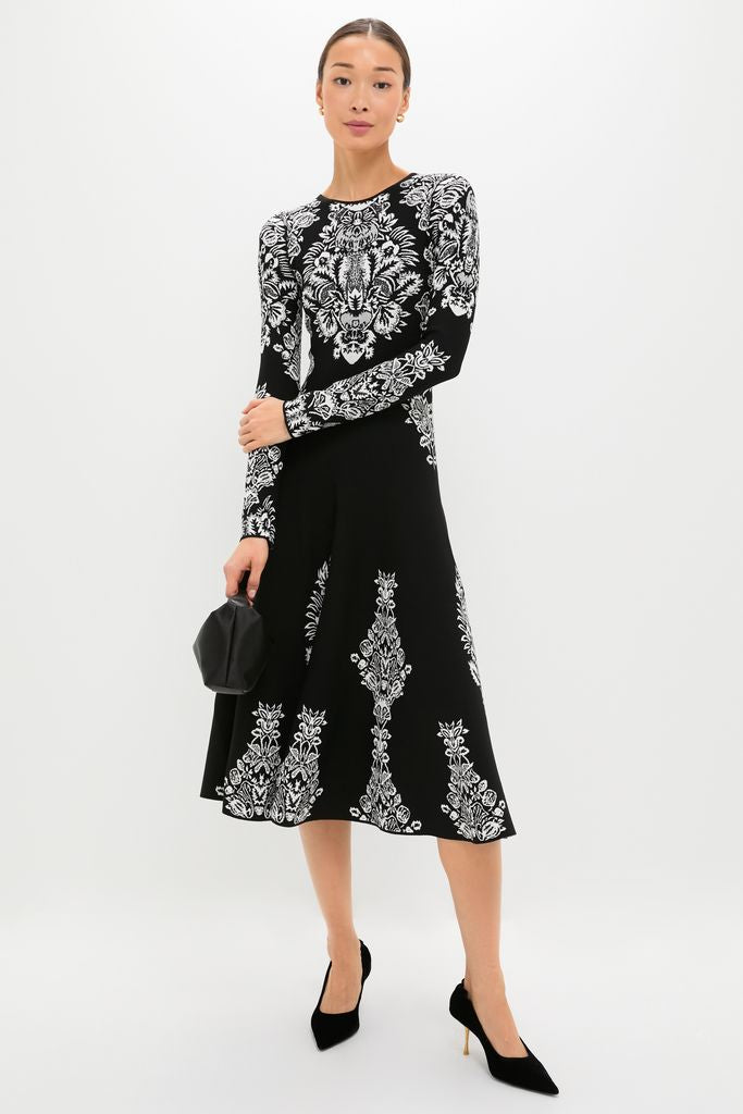 Noir Callista Dress: A classic, effortless midi dress featuring intricate white botanicals on black jacquard knit, paired with a black clutch and high-end pointed-toe heels.