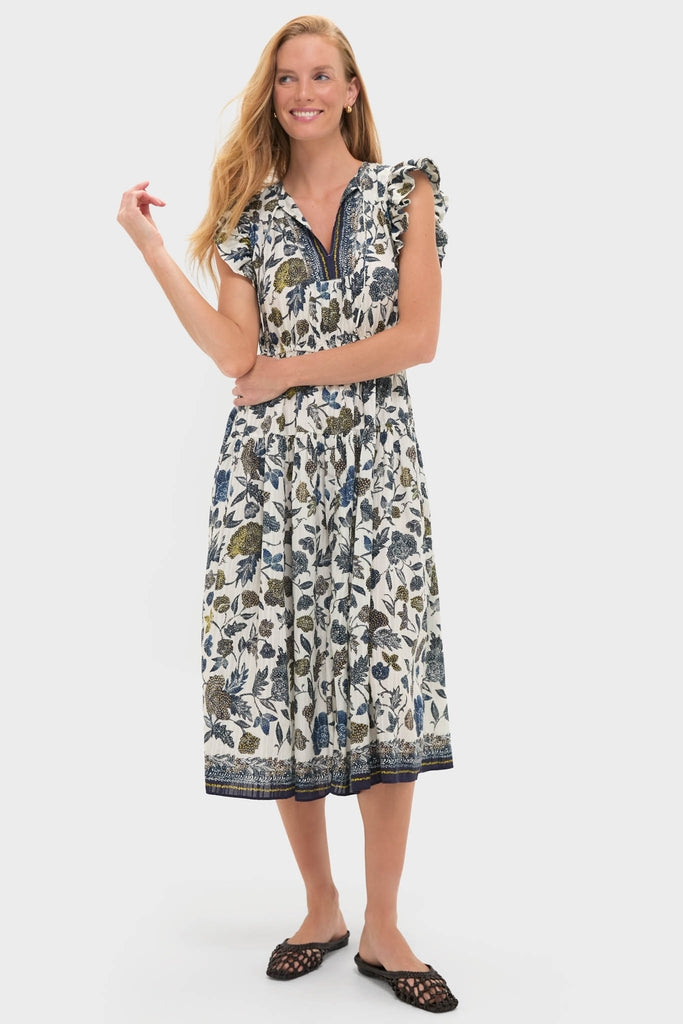 Porcelain Kairi Dress: A classic, effortless white cotton dress with a botanical print, V-neck, embroidered placket, ruffled cap sleeves, and gathered skirt, paired with black slip-on flats.