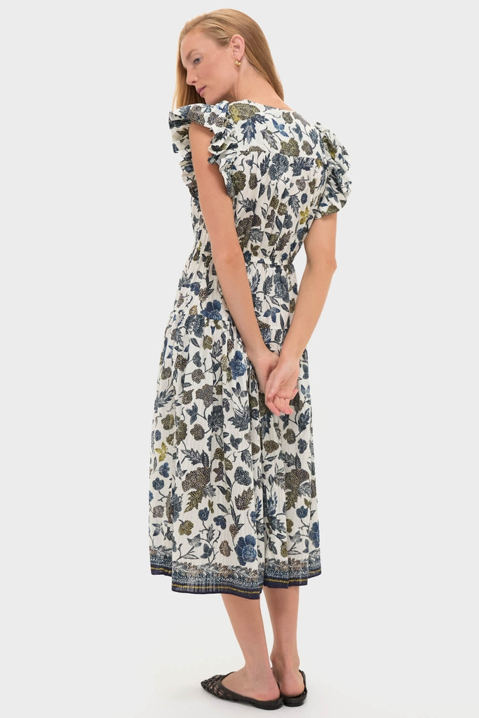 Woman models the classic Porcelain Kairi Dress, featuring flutter sleeves and a botanical print. Effortless elegance paired with fun black sandals, embodying high-end style.