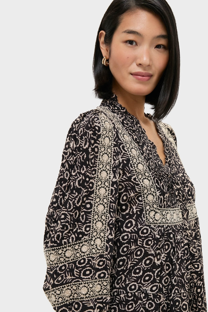 Young woman wearing the classic Multi Emmeline Print Long Sleeve Mini Tiered Dress, featuring an effortless geometric/floral design and elegant embroidered trim, paired with small gold hoop earrings.