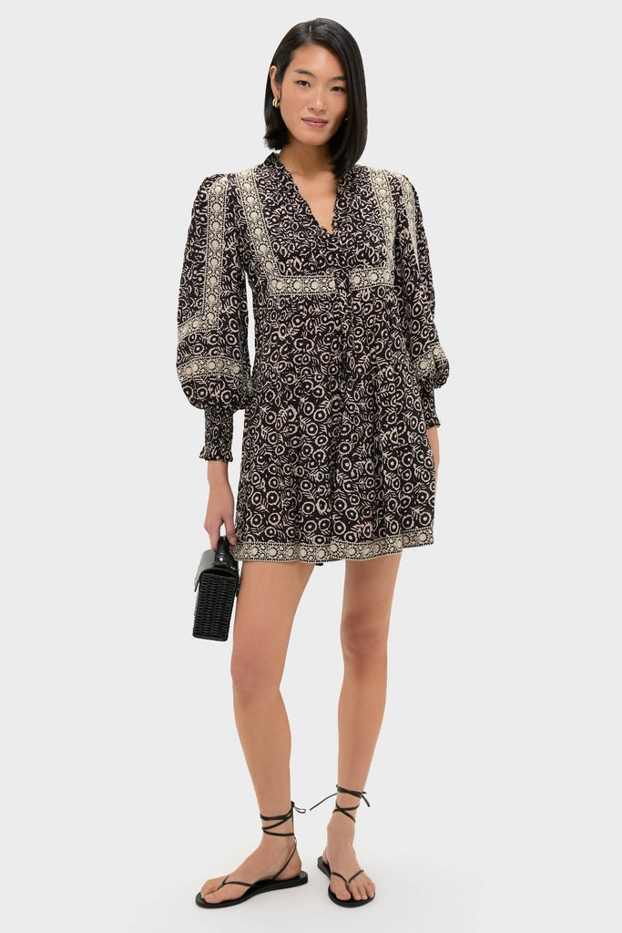 Model in a classic, effortless Multi Emmeline Print Long Sleeve Mini Tiered Dress with geometric print, styled with strappy sandals and a woven handbag for a fun, high-end look.