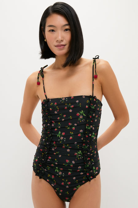 Woman wearing the Multi Katarina Print Tie Strap One Piece with floral design, ruched front, and crochet strawberry-tipped straps, embodying a classic, effortless, and fun high-end resort style.