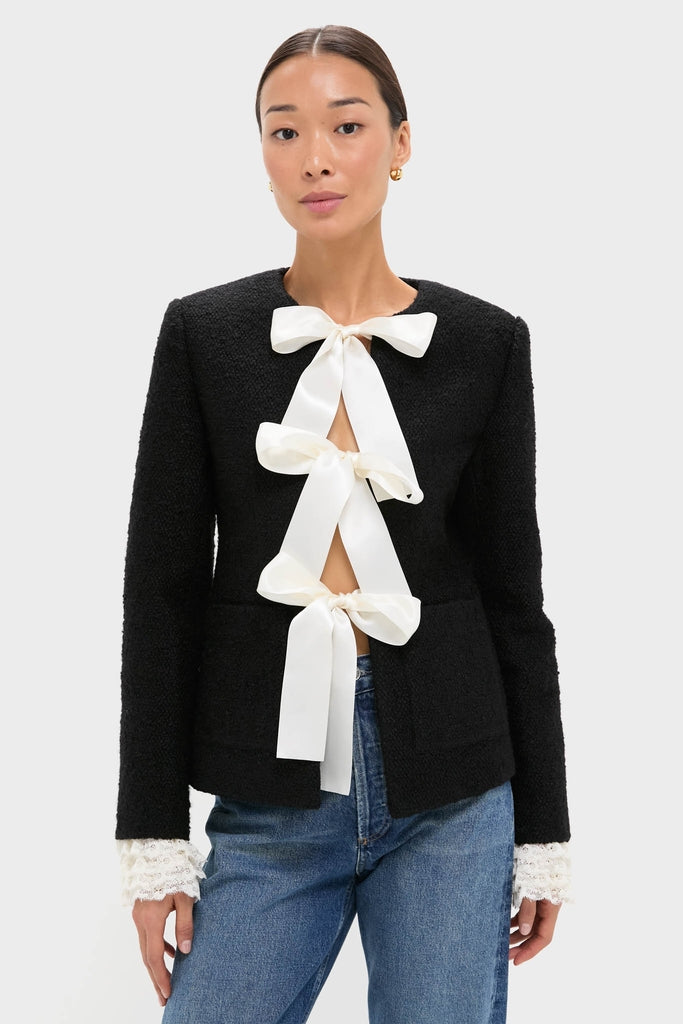 Model wearing the Black Seraphine Solid Bow Jacket with ivory ribbon bows, lace cuffs, and patch pockets, paired with jeans, embodying a classic, effortless, and high-end style.