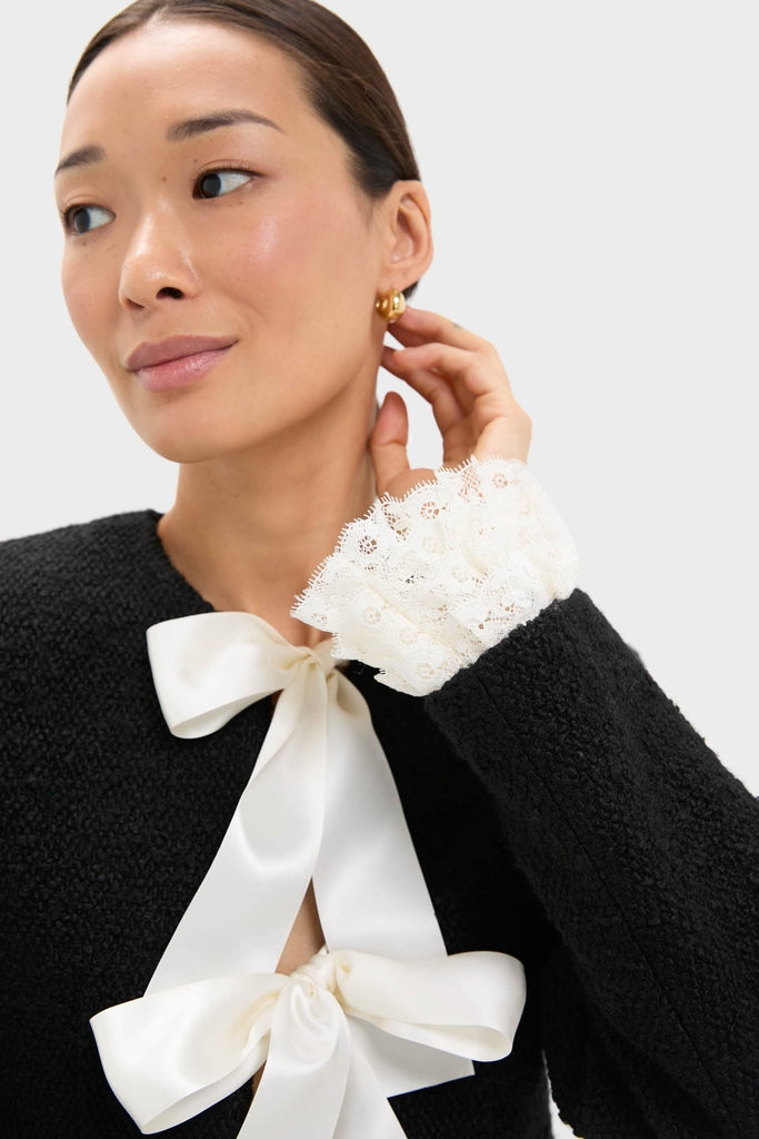 Woman wearing the Black Seraphine Solid Bow Jacket, featuring white satin bows and lace-trimmed cuffs, paired with gold hoop earrings for an effortless, high-end look.