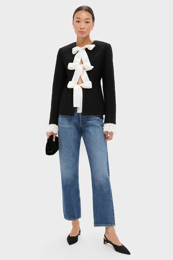 Model wearing the Black Seraphine Solid Bow Jacket with oversized satin bows, paired with classic mid-wash jeans and heels, creating an effortless, high-end look.