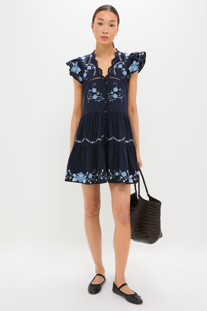 Young woman models the Exclusive Navy Edwina Embroidery Tunic Dress, showcasing its classic, effortless design with floral embroidery and flutter sleeves, paired with a black tote.