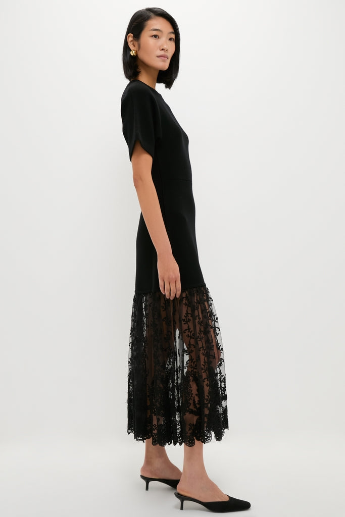 Woman in profile wearing the Black Diane Knit Lace Combo Knit Dress, featuring a classic fitted top and effortless lace skirt, paired with fun kitten-heel mules and high-end gold hoop earrings.