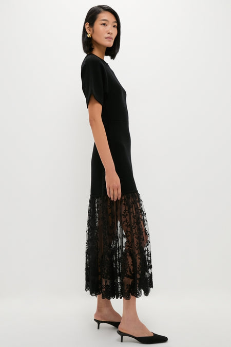 Woman in profile wearing the Black Diane Knit Lace Combo Knit Dress, featuring a classic fitted top and effortless lace skirt, paired with fun kitten-heel mules and high-end gold hoop earrings.