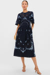 Exclusive Navy Edwina Embroidery Midi Dress features classic floral embroidery, intricate lace insets, and effortless bell sleeves, styled with a fun straw clutch and high-end sandals.