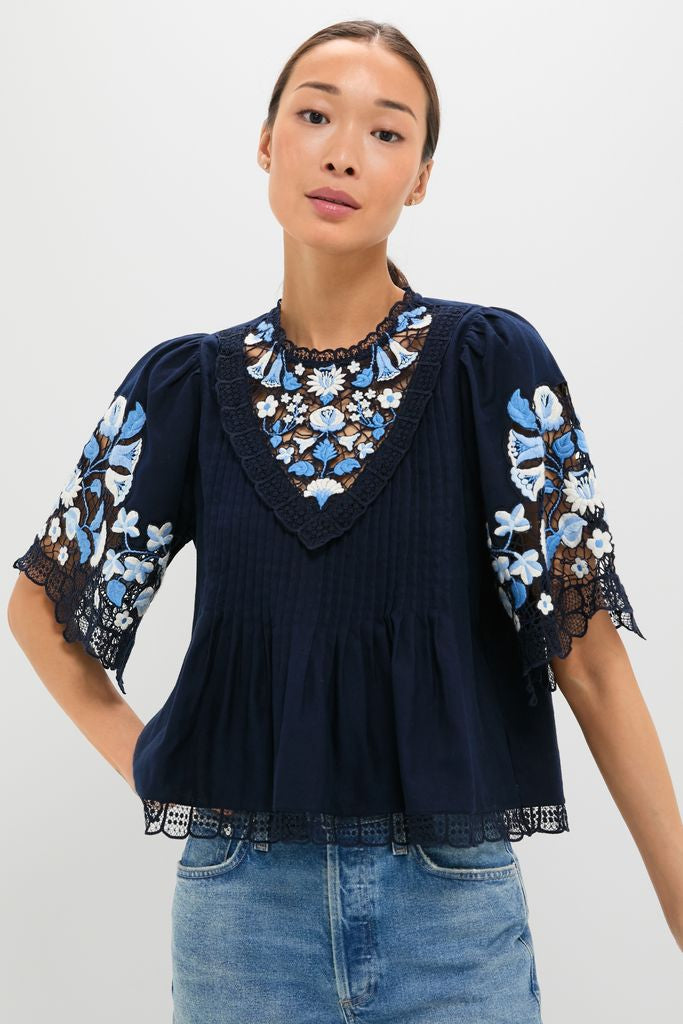 Exclusive Navy Edwina Embroidery Short Sleeve Top with intricate floral lace, pleats, and bell sleeves, paired with light-wash jeans for a classic, effortless elegance.