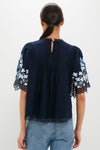 Exclusive Navy Edwina Embroidery Short Sleeve Top: Classic lace-trimmed blouse with floral embroidery, puff shoulders, and pleats, styled effortlessly with light-wash jeans for a fun, high-end look.