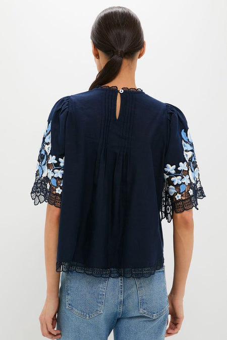 Exclusive Navy Edwina Embroidery Short Sleeve Top: Classic lace-trimmed blouse with floral embroidery, puff shoulders, and pleats, styled effortlessly with light-wash jeans for a fun, high-end look.