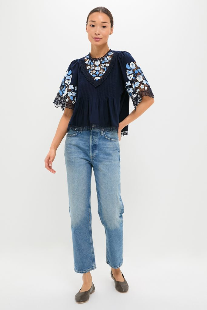 Exclusive Navy Edwina Embroidery Short Sleeve Top, a classic, effortless blouse with intricate floral embroidery and bell sleeves, paired with light-wash jeans for a high-end, fun look.