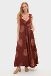 Woman models the Rust Toye Dress, a classic, high-end maxi with a knotted bust, appliqué leaf straps, smocked empire waist, and tropical print, embodying effortless and fun style.