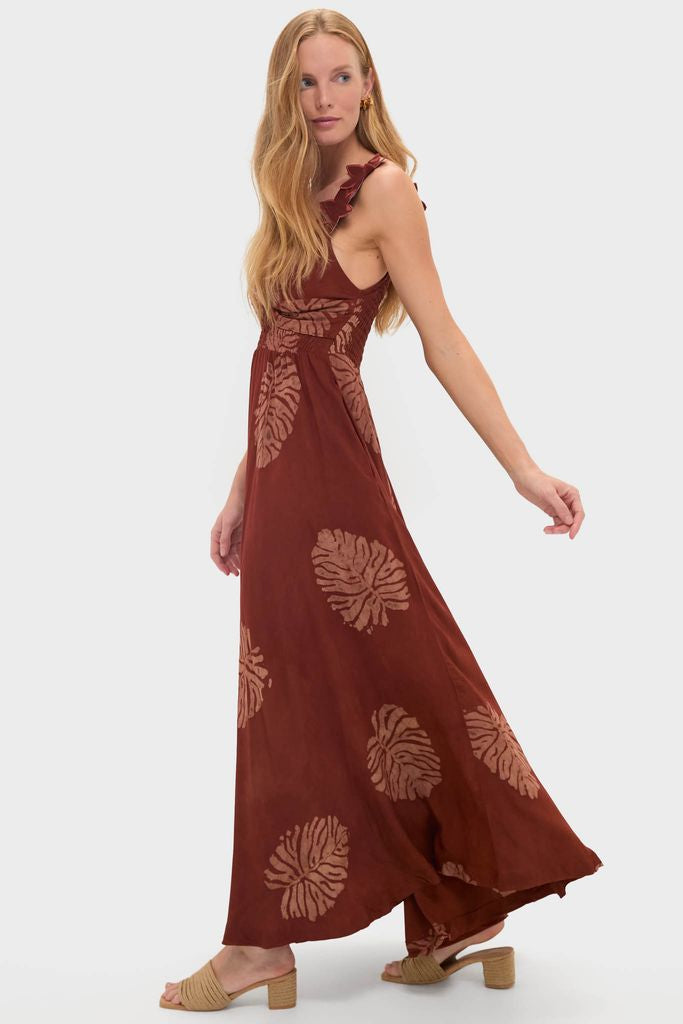 Model wearing the Rust Toye Dress, a classic, effortless maxi with a scoop neckline, ruffle-trimmed straps, and a flowing skirt featuring oversized leaf prints. Paired with low-block-heel woven sandals.