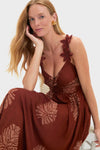 Woman models the Rust Toye Dress, a classic, ankle-length piece with leaf motifs. Features include wide straps with flower appliqués and an elastic waist, embodying effortless, high-end style.