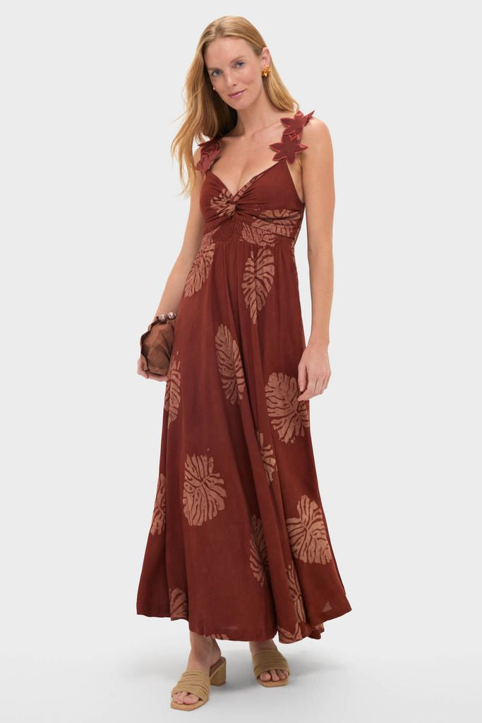 Model wearing the Rust Toye Dress, a classic maxi with oversized leaf prints and bust knot detail, styled with a brown clutch and gold-tone earrings for an effortless, high-end look.