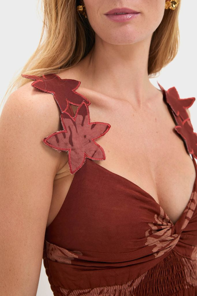 Woman wearing the classic Rust Toye Dress with broad straps detailed in appliqué flowers, featuring an effortless gathered knot at the bust, embodying Tuckernuck's fun, high-end style.