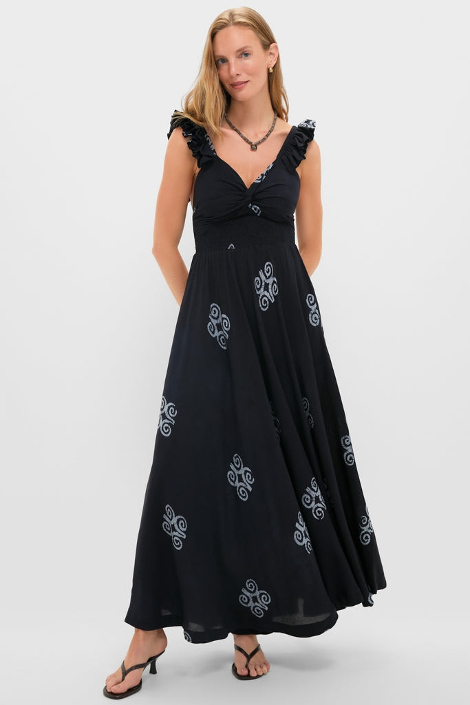 Woman wearing the classic Black Ibukun Dress with subtle swirl motifs, featuring a gathered waist and ruffled straps, paired with black heeled sandals for an effortless, high-end look.