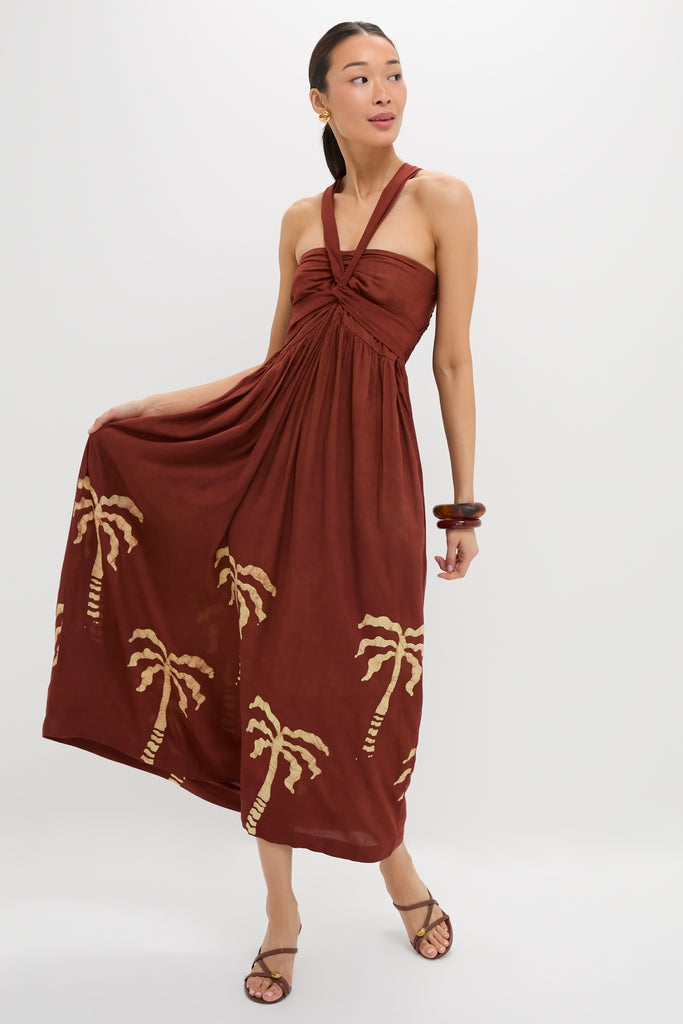 Model wearing the Rust Anike Dress, a classic, strapless, high-end piece with a knotted halter neckline and an effortless, fun palm-tree print.
