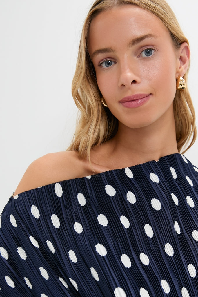 Young woman wearing the Small Dot Deep Lake Cami Top, showcasing its classic, high-end off-the-shoulder design with effortless, fun navy-blue polka dots and gold hoop earrings.