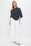 Model wearing the Small Dot Deep Lake Cami Top, a classic navy polka dot one-shoulder blouse, paired with effortless high-waisted white trousers and tan sandals.