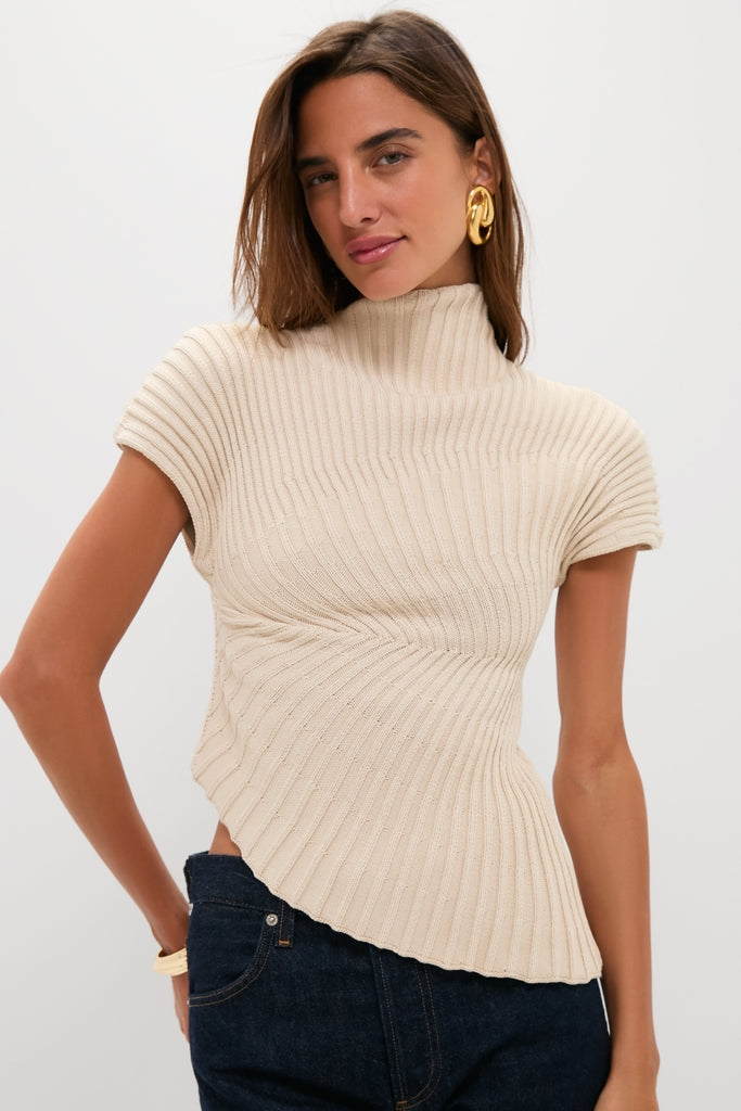 Model wears Beach Annemie Top, a classic, asymmetrical knit with a mock neck and flared sleeves, paired effortlessly with dark indigo jeans and high-end chunky gold accessories.