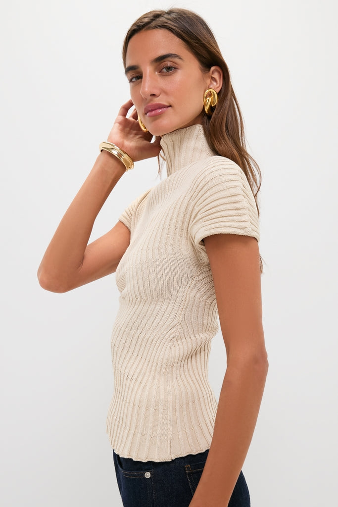 Young woman in an effortless cream Beach Annemie Top, showcasing an asymmetrical design and stitch detailing, paired with dark jeans and gold accessories for a classic, high-end look.