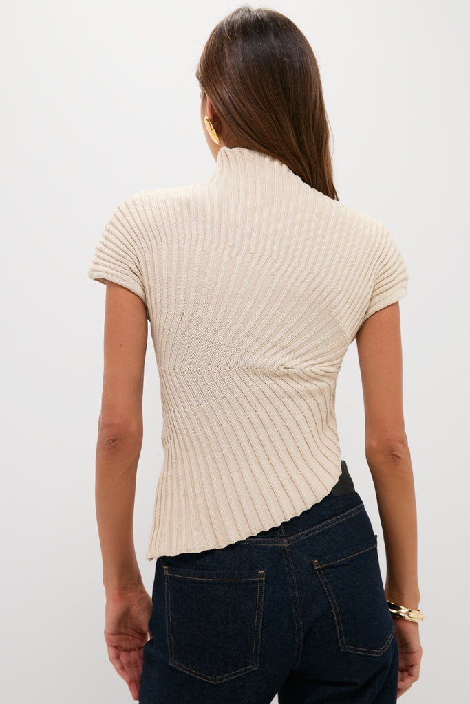 Back view of the classic Beach Annemie Top, featuring an effortless asymmetrical design with radial stitching, flared sleeves, and a mock neck, paired with dark jeans for a high-end, fun look.