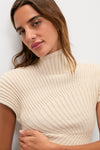Woman wearing the Beach Annemie Top, a classic, high-end ribbed knit with an asymmetrical turtleneck and flared cap sleeves, exuding effortless style and fun sophistication.