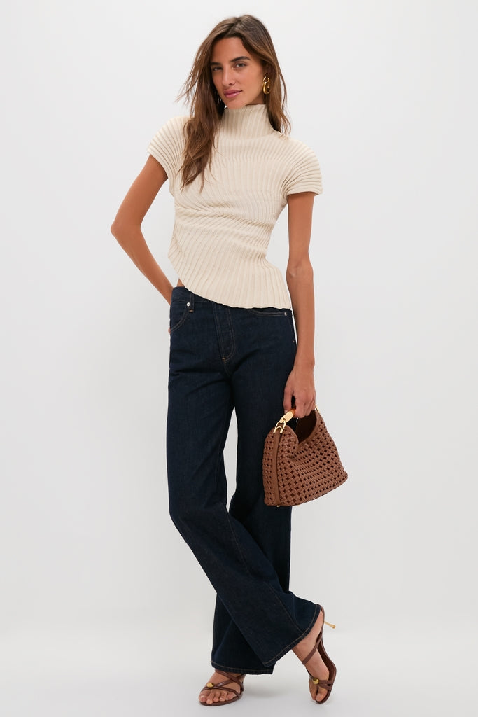 Model wearing the classic Beach Annemie Top with an asymmetrical neckline, paired with high-waisted jeans. Effortless, fun style with high-end gold accessories and strappy sandals.