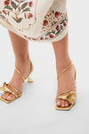 Brass Ria Sandals: Classic metallic gold sandals with an effortless sculptural knot detail, square toe, and slender ankle straps, embodying a fun, high-end style.