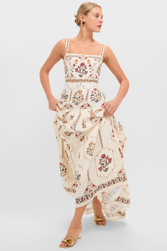 Model wearing a cream botanical dress and classic Brass Ria Sandals, exuding effortless elegance with fun, high-end style through gold hoops and strappy gold heels.