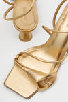 Brass Ria Sandals: Classic metallic-gold strappy heeled sandals with square-toed footbed and sculptural block heel, exuding effortless fun and high-end style.