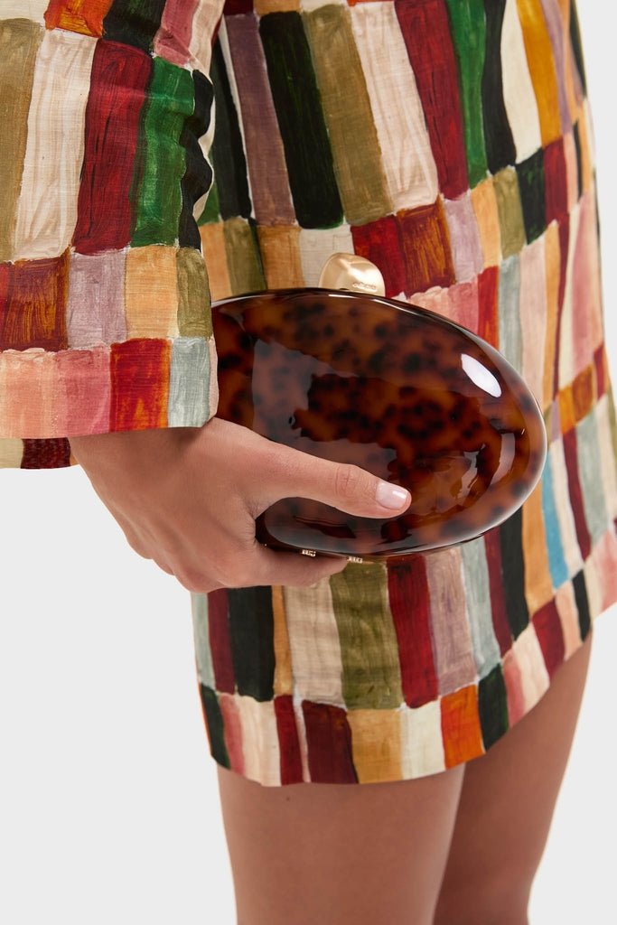 Caramel Tortoise Eviana Clutch, a classic, high-end accessory with a gold-tone clasp, effortlessly held by a model, exuding sophistication and fun for any RSVP.