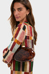 Woman in a multicolored dress holds the Caramel Tortoise Eviana Clutch, a classic, high-end acrylic purse with a gold-tone clasp and chain, exuding effortless sophistication.