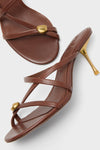 Saddle Valeska Sandals: Classic brown leather sandals with crisscross straps, a chic gold stud, and an effortless sculptural stiletto heel. Perfect for high-end, fun style.