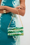 Person wearing a teal dress holds the classic Sage Aura Clutch, a high-end, sculptural bag with a marbled finish and gold-tone chain, embodying effortless, fun style.