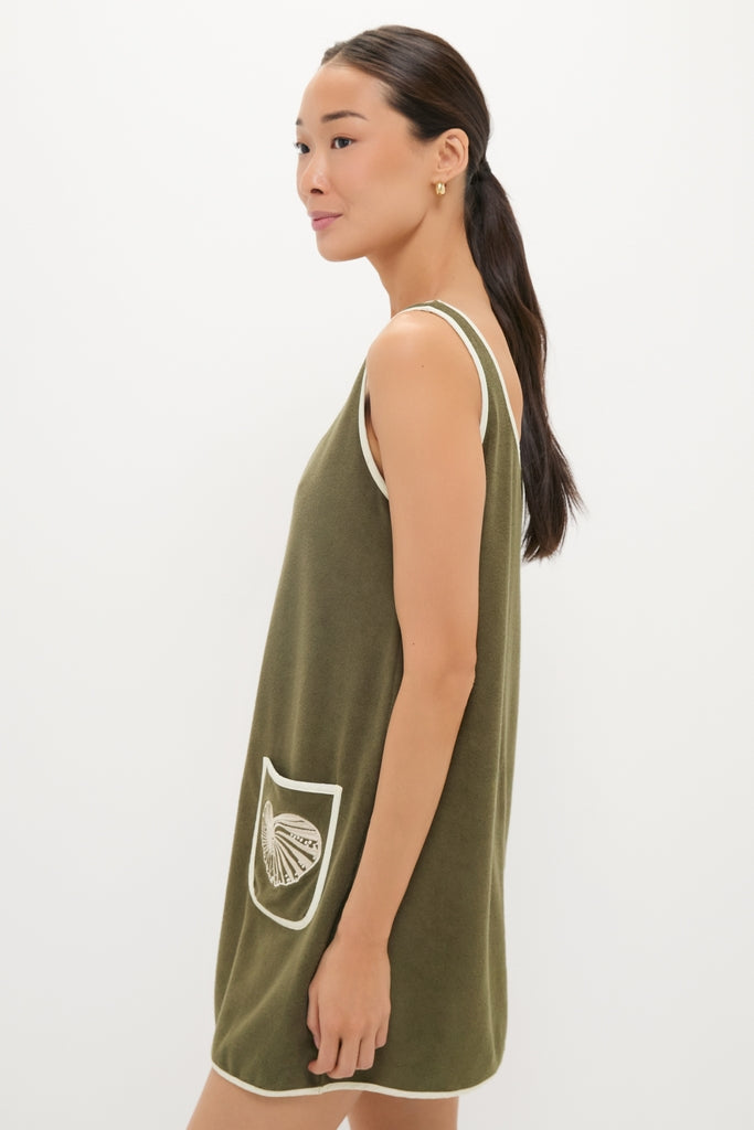 Slim person in profile wearing the Fern Embroidered Mini Terrycloth Dress Coverup. This classic, effortless olive-green dress features white piping and a fun seashell pocket, exuding high-end style.