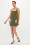 Woman models the Fern Embroidered Mini Terrycloth Dress Coverup, a classic, effortless olive-green sleeveless mini dress with white-trimmed details and seashell patch pockets, paired with strappy sandals.