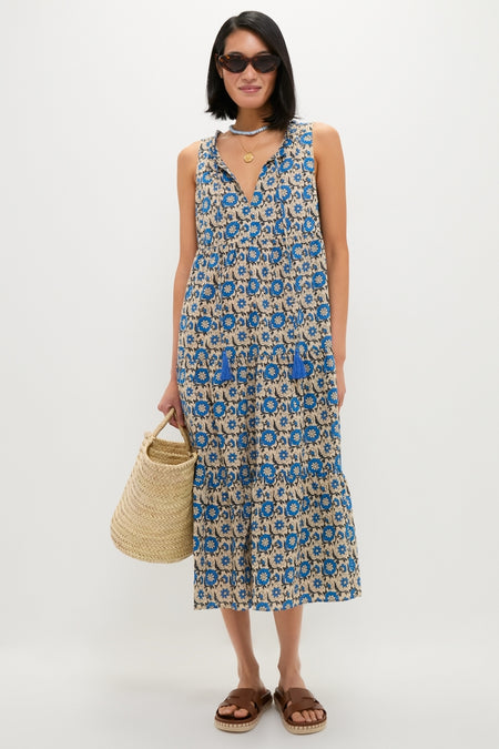 Model wearing the classic Cobalt Primrose Salty Paloma Caftan, an effortless beige midi dress with vibrant blue florals, paired with chic tortoiseshell sunglasses and a fun straw tote.