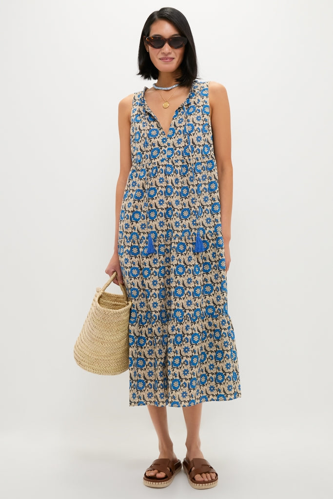 Model wearing the classic Cobalt Primrose Salty Paloma Caftan, an effortless beige midi dress with vibrant blue florals, paired with chic tortoiseshell sunglasses and a fun straw tote.