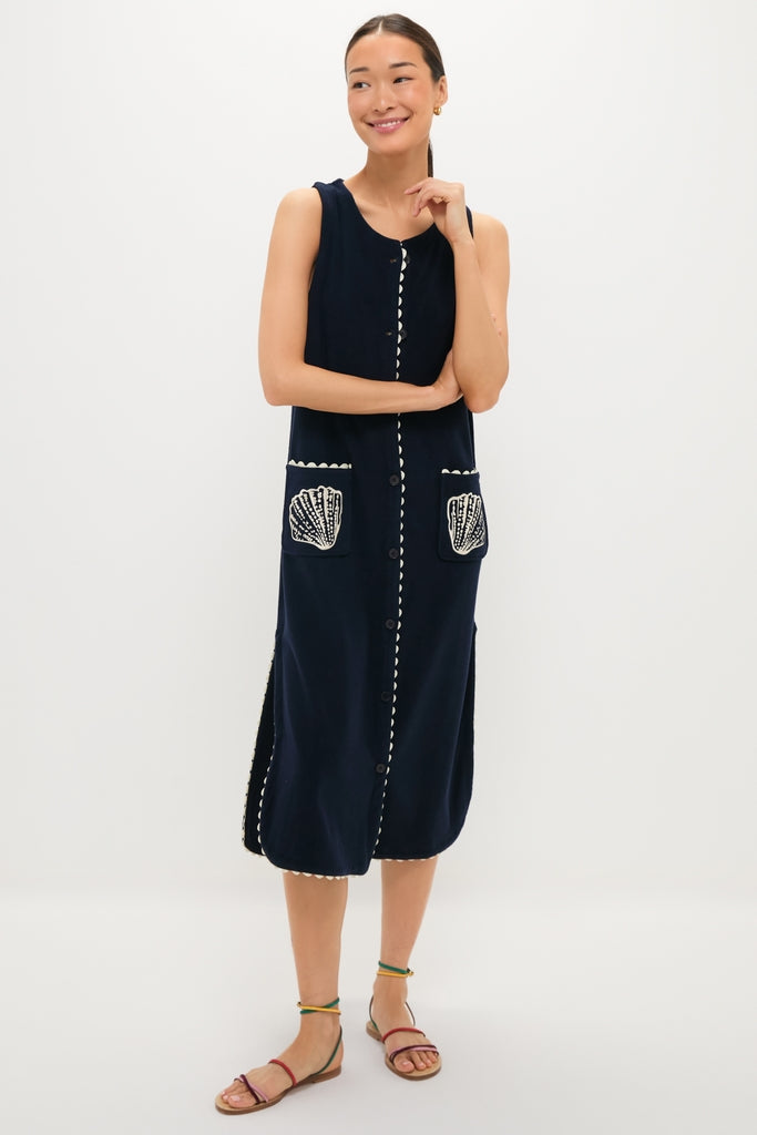 Young woman in a classic, navy embroidered Bermuda terrycloth caftan with shell motifs and scalloped trim, exuding effortless, high-end style, paired with fun, earthy strappy sandals.