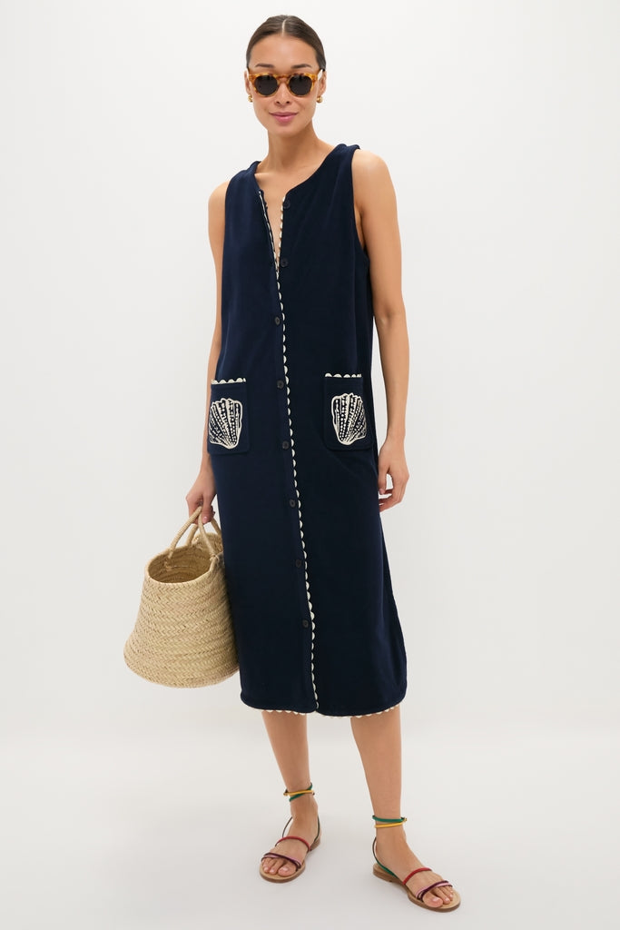 Woman models the Navy Embroidered Bermuda Terrycloth Caftan, featuring scalloped trim, shell-embroidered pockets, and a button-front, paired with a woven tote and stylish sandals for an effortless, high-end look.