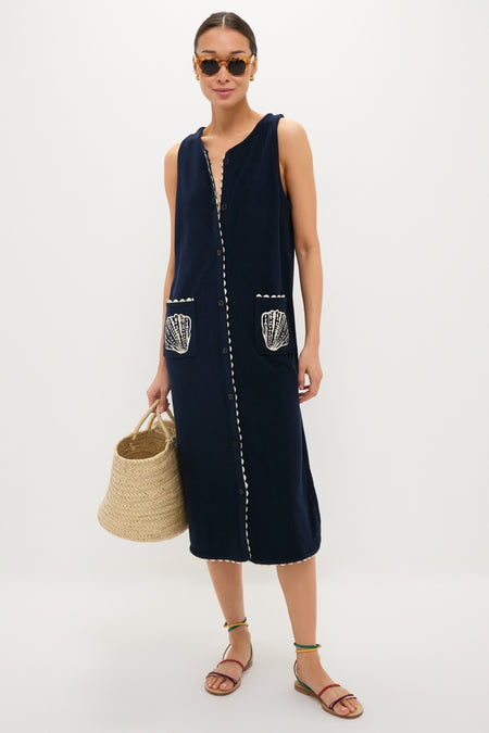 Woman models the Navy Embroidered Bermuda Terrycloth Caftan, featuring scalloped trim, shell-embroidered pockets, and a button-front, paired with a woven tote and stylish sandals for an effortless, high-end look.