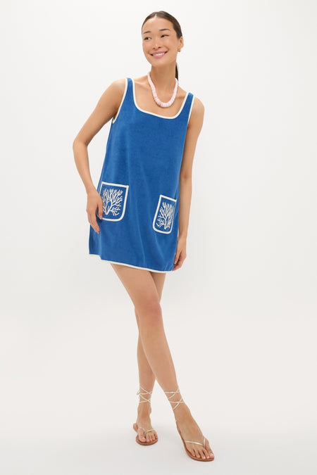 Woman in Cobalt Embroidered Terrycloth Dress Coverup, featuring classic white coral motifs and pockets, exuding an effortless, fun, high-end vibe with strappy sandals and a chunky necklace.