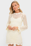 Ivory Knit Tamara Mini Dress: A classic, open-knit crochet design with scalloped edges, effortlessly styled with pom-pom earrings for a fun, high-end look.
