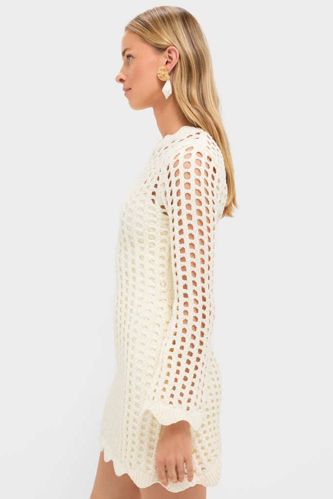 Woman in profile wearing the Ivory Knit Tamara Mini Dress, a classic, open-weave crochet mini with scalloped hem and long sleeves, accessorized with statement earrings, embodying effortless, high-end style.