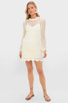 Model in an Ivory Knit Tamara Mini Dress, featuring an open-knit design with long sleeves and scalloped hem, embodying classic, effortless style with a fun, high-end appeal.