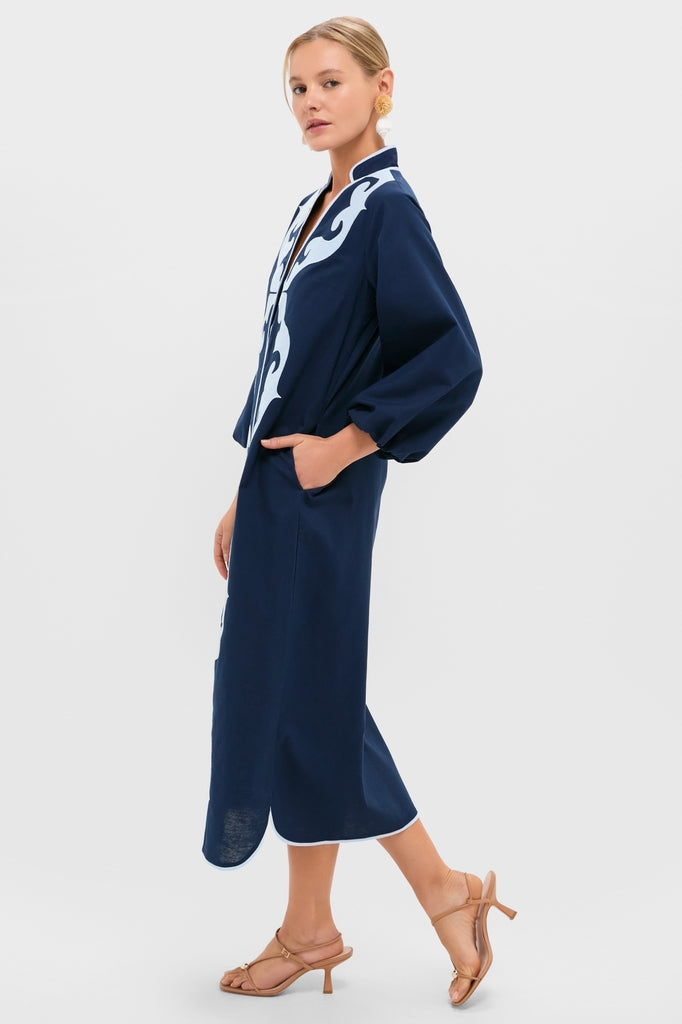 Model in profile wearing the classic Navy & Baby Blue Embroidered Teresa Caftan with billowed sleeves and scalloped hemline, paired with tan strappy sandals and gold earrings.